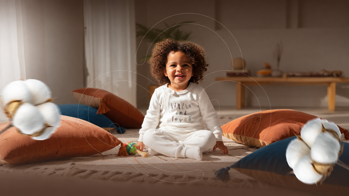 Smiling child in a white Plantas Kids outfit surrounded by cushions