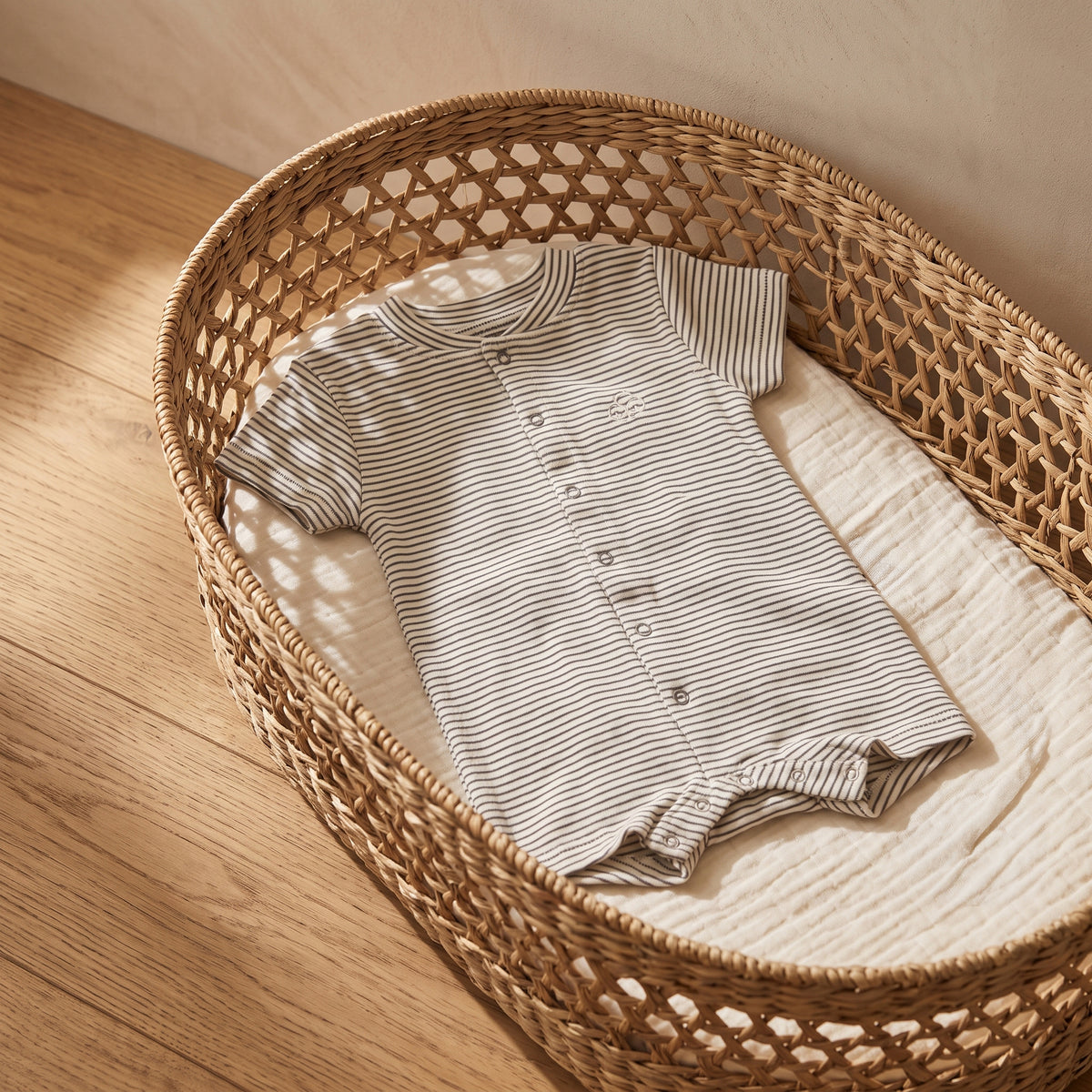 Charcoal-striped short-sleeve romper laid flat in a woven basket