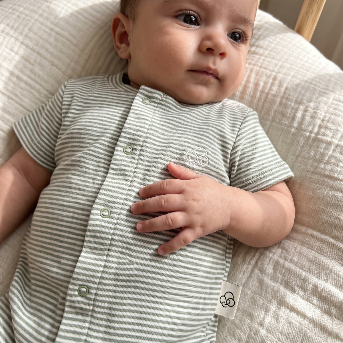 Close view of a baby wearing the green-striped romper, showing its front snaps