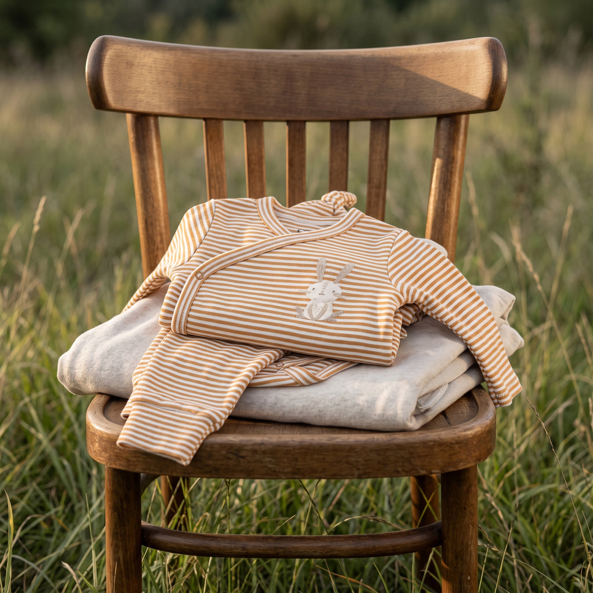 Folded camel-striped Little Bunny kimono set displayed on a wooden chair outdoors
