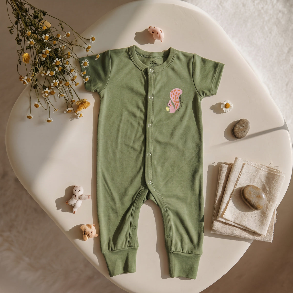 Olive-green Olive Grove jumpsuit laid flat, showing short sleeves, front snaps and a squirrel detail