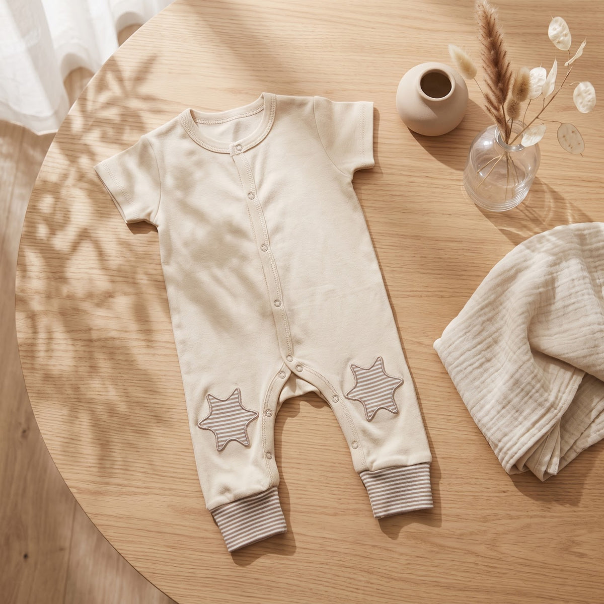 Beige Stars jumpsuit laid flat, showing short sleeves, striped cuffs and star patches