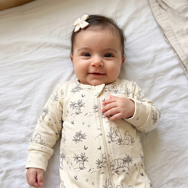 Smiling baby lying on a bed in the PLANTAS Kids Panda Cotton Jumpsuit in White Alyssum