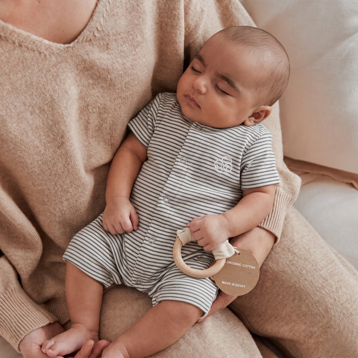 Baby held by an adult while wearing the charcoal-striped short-sleeve romper