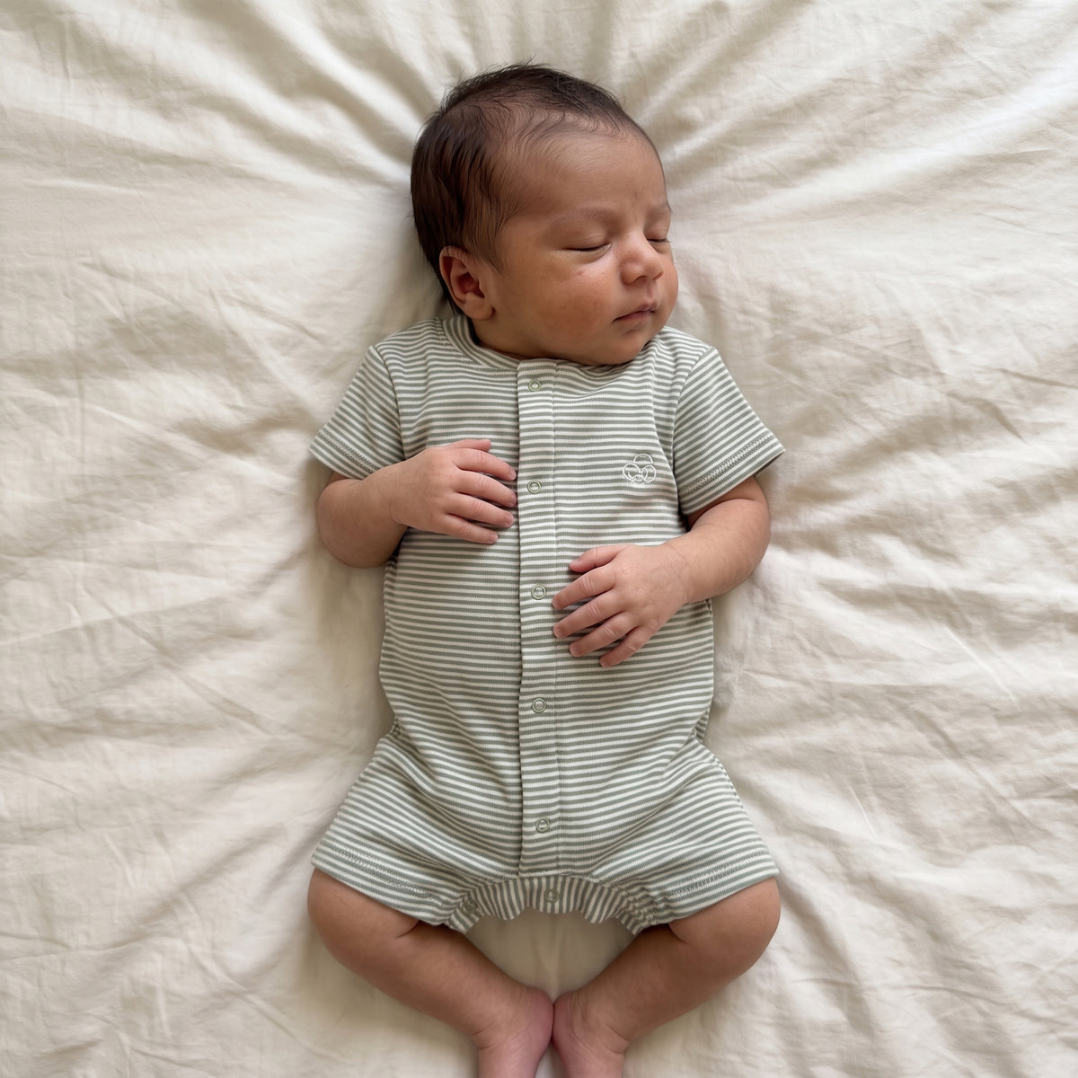 Baby lying on a cream bed wearing the green-striped short-sleeve romper