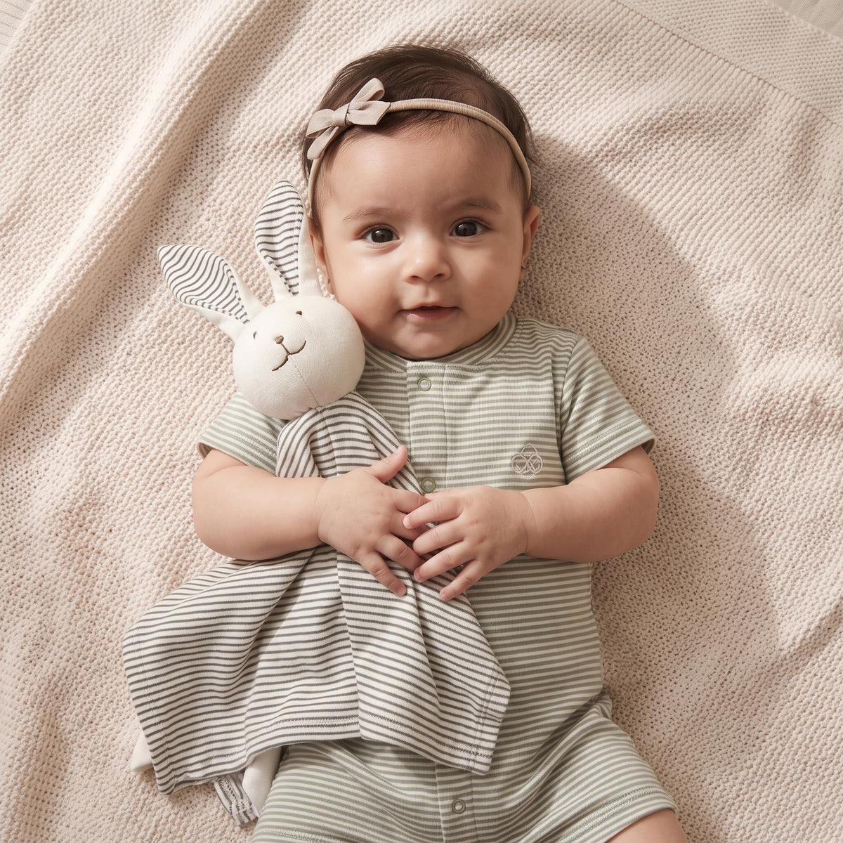 Baby holding the charcoal-striped Little Bunny comforter toy against a striped outfit