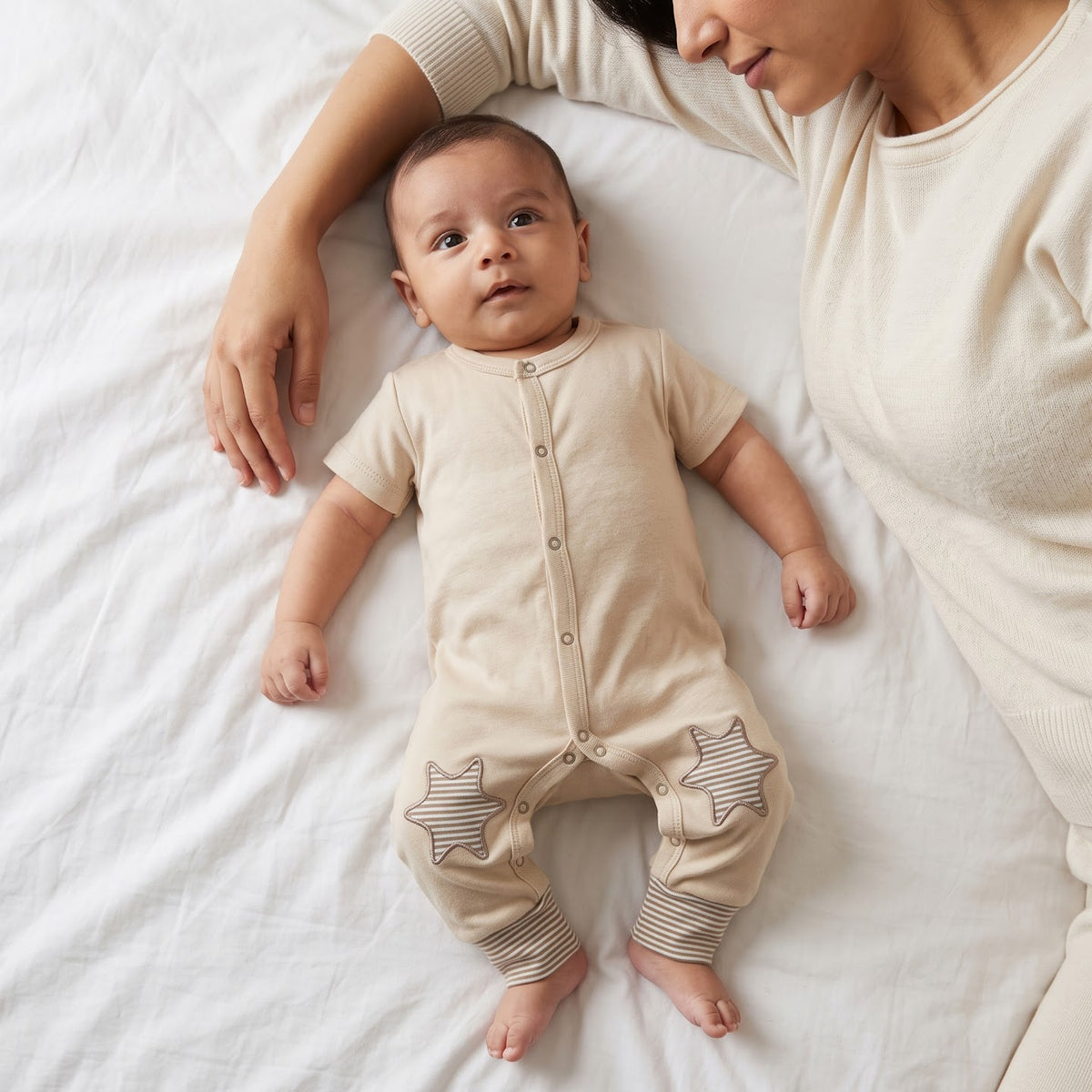 Baby wearing the beige Stars short-sleeve jumpsuit beside an adult